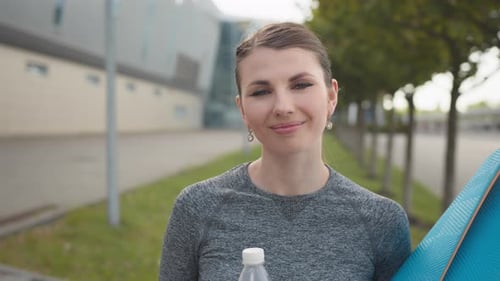 Smiling Woman Holding Yoga Mat and Water Bottle