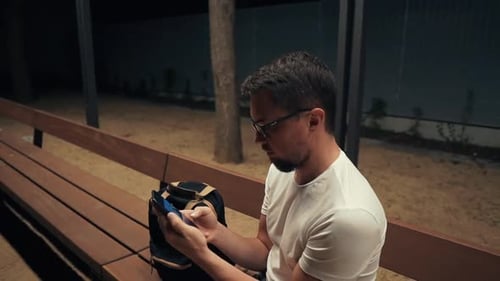 Alone Man Is Sitting Alone in Park in Evening, Looking for a Net for Phone