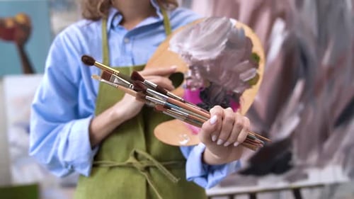 Smiling Woman Holds Paintbrushes and Palette in Studio