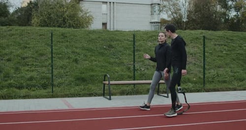 Side View of Young Woman Talking To Man with Prosthetic Running Blade Outdoors
