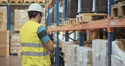 Logistics worker wearing a helmet working in a large warehouse checking inventory