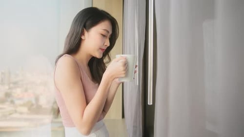 Young Woman Drinking Coffee in Apartment Overlooking City