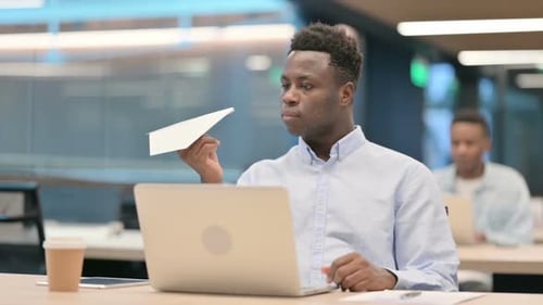 Young Man Holds Paper Airplane at Office Desk