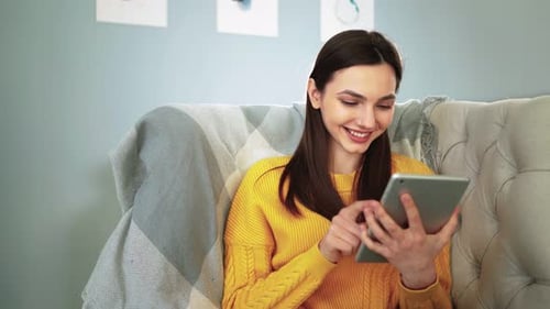 Woman Smiles Using Tablet Device on Couch