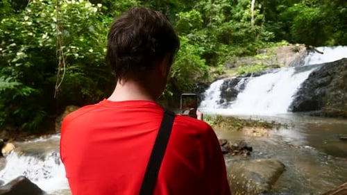 Man Photographing Waterfall in Lush Green Tropical Forest