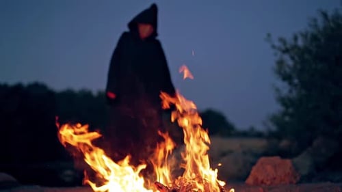 Blurred Figure in Robe Standing Behind Bonfire