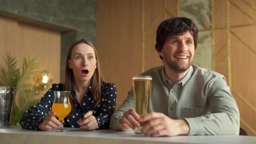Young Couple is Rooting for Their Favorite Sports Team in a Bar Watching a Match Online
