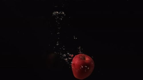 Pomme rouge qui tourne dans l'eau avec des bulles sur fond noir, fruits tombant dans l'eau