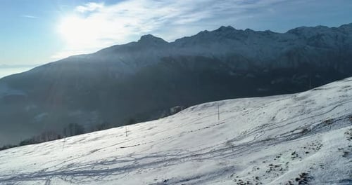 Backward Aerial Top View Over Winter Snowy Mountain with Ski Tracks in Sunny Day with Clouds