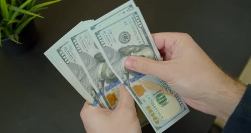 Close-up of a Businessman's Hands Counting Hundred Dollar Bills at a Black Table.