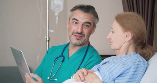 Doctor Reviews Tablet With Senior Patient in Hospital