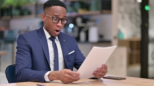 African Businessman Celebrating Success on Documents in Office