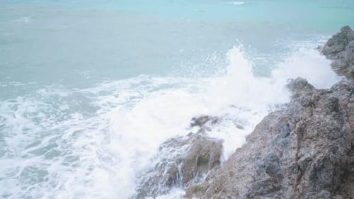 Slow motion waving blue sea hitting rock stone on beach