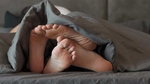 Feet of Couple Under Blanket in Bed