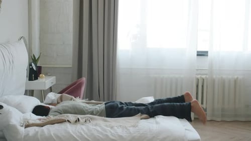 Man Jumps onto Bed in Bright Bedroom