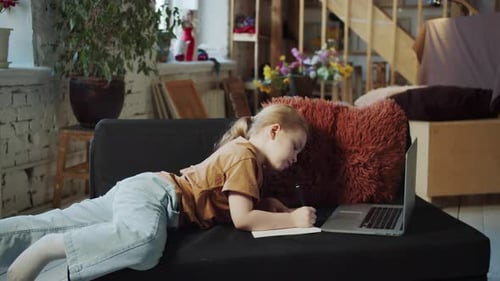 Teenager macht Hausaufgaben, während er auf der Couch vor einem Laptop liegt
