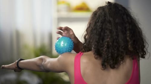Fit jeune femme roulant la balle de massage sur le bras, vue de derrière, relaxation