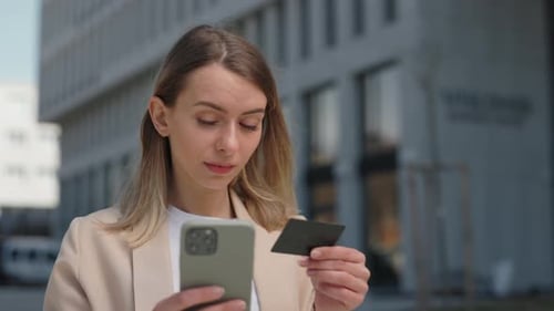 Woman with Credit Card and Phone Making Purchasing Outdoors