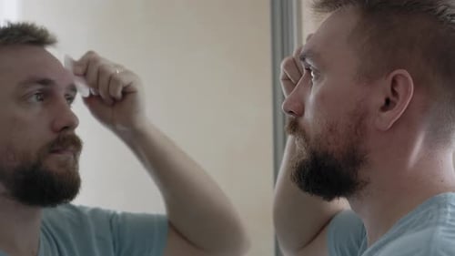 Man Massaging Forehead with Facial Tool in Mirror