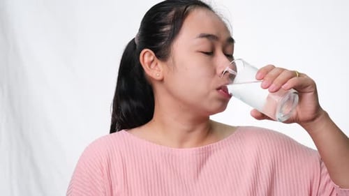 Happy woman drinking water from glass on white background in studio. Healthy lifestyle
