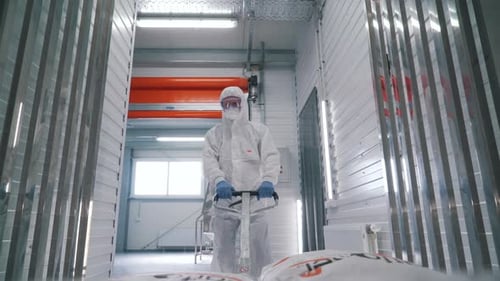 Worker in Protective Suit Moving Bags in Factory