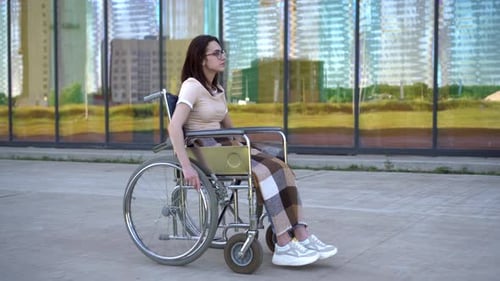 Young Woman in a Wheelchair. A Girl Rides in a Wheelchair Against the Background of a Glass Building