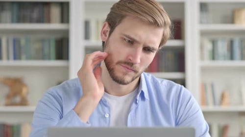 Man Rubbing Neck at Desk Working on Laptop