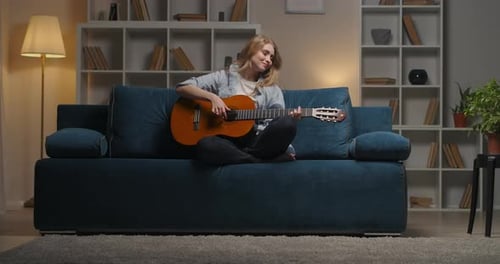 Blonde Woman Plays Guitar on Blue Sofa