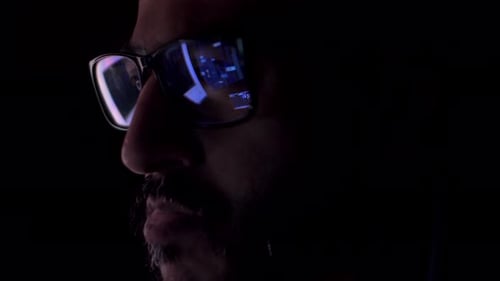 Ojos masculinos en anteojos a altas horas de la noche desplazándose frente a la computadora portátil. Programador, programador o desarrollador u