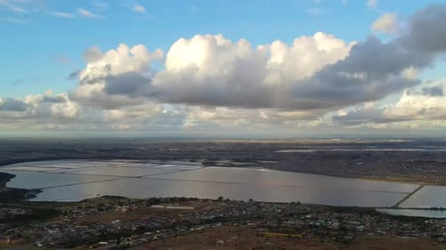Drone Flying Over Residential Area with Clouds Hovering and Salt Pan in Background