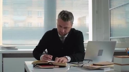 Man Writing in Notebook at Desk in Office