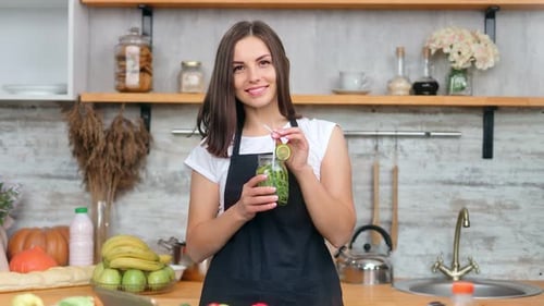 Smiling Woman Holding Refreshing Drink in Bright Kitchen