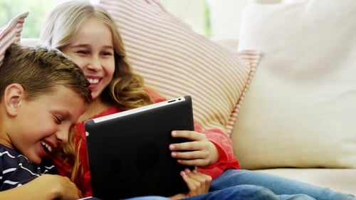 Smiling Children Using Tablet Together on Couch