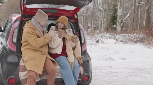 Young Couple Drinking Hot Tea at Car Trunk