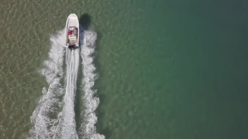 Von oben nach unten ragende Antenne eines weißen Schnellboots in einer flachen, sonnengrünen Lagune