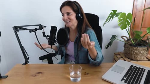 Mature woman recording a podcast using microphone and laptop from her home studio