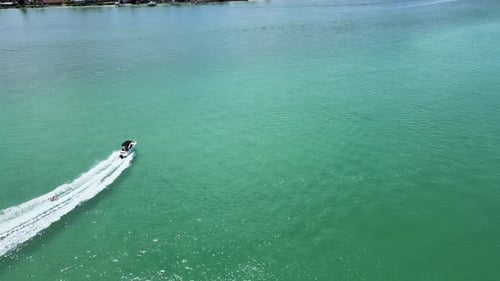 The camera is flying across the ocean and lowering in altitude as a boat pulling a towable inflatabl