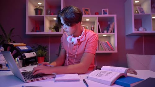 Teen Student Studying with Laptop and Textbook at Night