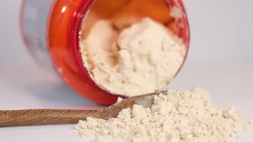 Protein Powder Spilling From Container With Wooden Spoon