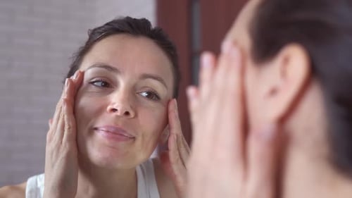 Woman Massaging Face in Bathroom Mirror