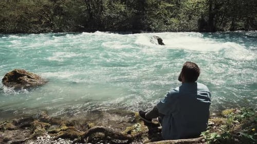Alleiner bärtiger Mann sitzt am Ufer und schaut bei Tag nachdenklich auf den Fluss