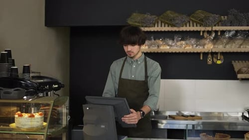 Young Cashier in Apron Typing on Touch Screen in Bakery Store