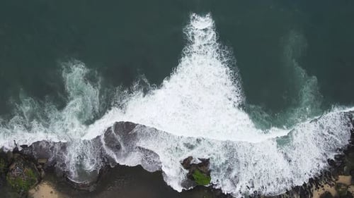 Luftaufnahme von oben auf riesige Meereswellen, die am Korallenstrand zusammenbrechen und schäumen