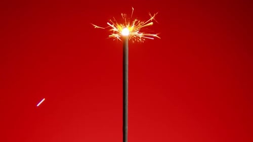 Sparkler Emitting Sparks Against Red Backdrop