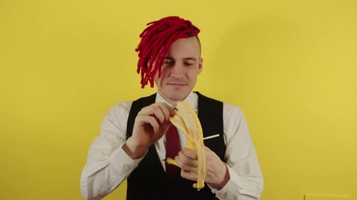 Young Man in White Shirt Vest and Tie Peeling Banana on Yellow Background in Studio