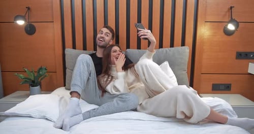 Junges Paar macht ein Selfie auf einem Smartphone Mann und eine Frau liegen auf dem Bett und drehen ein Video auf einem