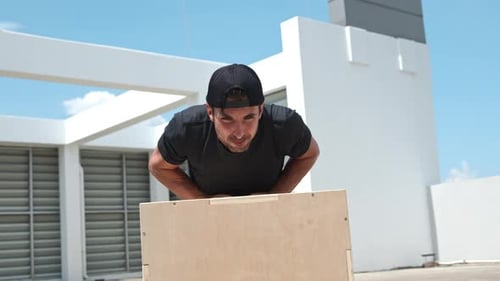 Handsome sports man doing close grip push up exercise on wood box outdoors
