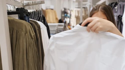 Young Woman Examines a White Longsleeved Shirt in a Store