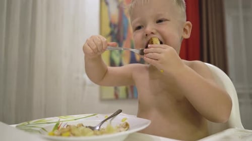 Child Eating Food with Spoon in High Chair