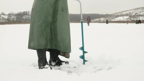 Fischer bohrt Eisloch auf gefrorenen Fluss